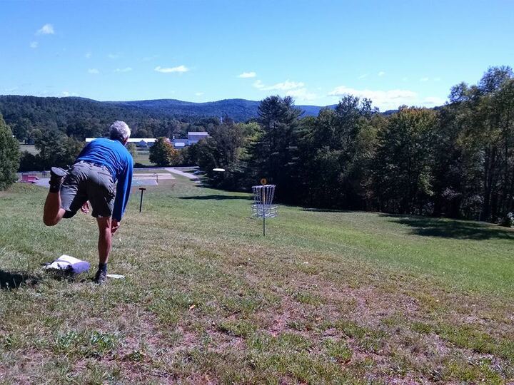 Disc golfer putting toward a basket on an open fairway