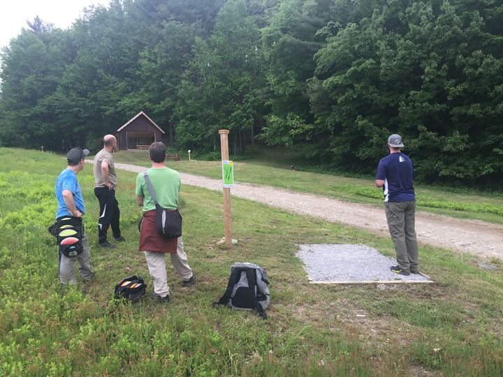 Disc golfers walking from a tee on a wooded fairway